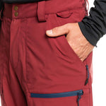 Quiksilver Utility Shell Pant 2023 - A pair of red snow pants with a zippered pocket on the side and two brown buttons at the waistband.