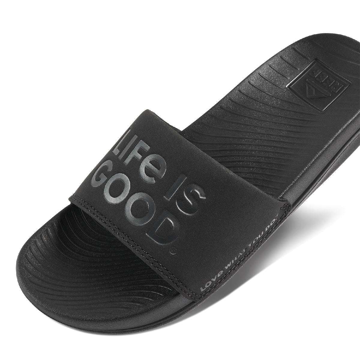 Reef X Life Is Good Women's Slide 2022 - A pair of black slide sandals with a logo on the strap.