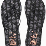 Reef Women's Bliss-Full Sandal 2020 - A pair of black sandals with a strap across the foot and a toe post, featuring a pineapple pattern on the straps.