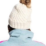 Roxy Women's Blizzard Beanie 2022 - A cream-colored beanie with a cable-knit pattern and a brown faux fur pom-pom on top.