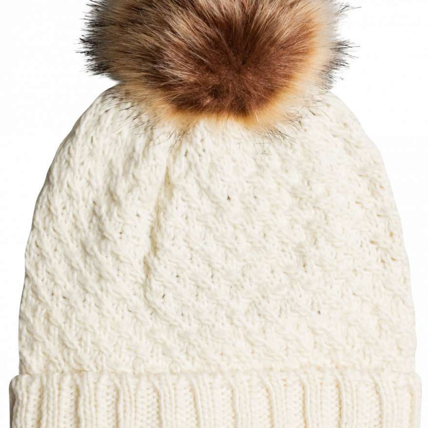 Roxy Women's Blizzard Beanie 2023 - A cream-colored beanie with a cable-knit pattern and a large, fluffy brown faux fur pom-pom on top.