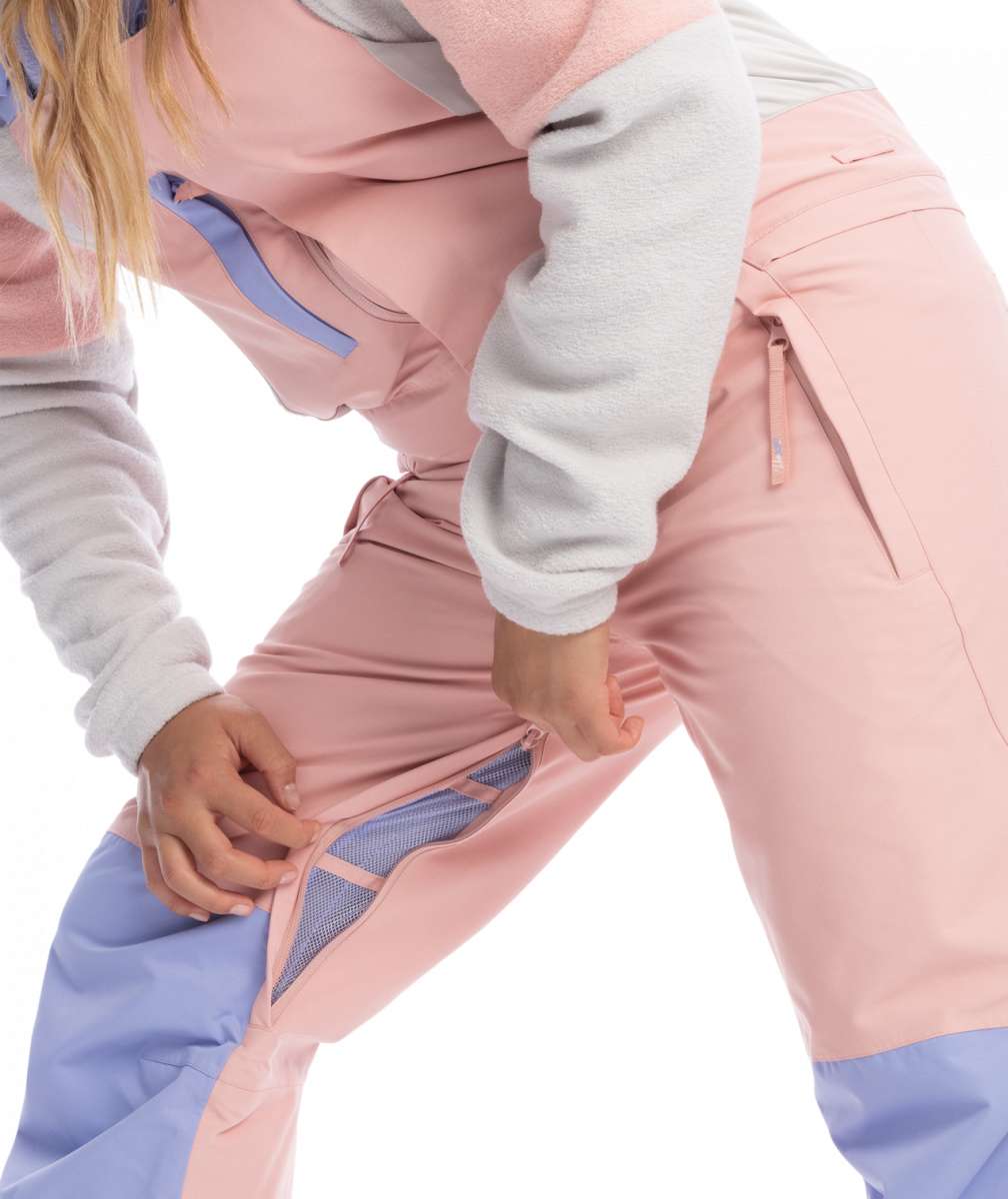 Roxy Women's Chloe Kim Bib Pant 2023 - A pair of pink snow pants with a blue stripe down the side and a zippered pocket on the thigh.