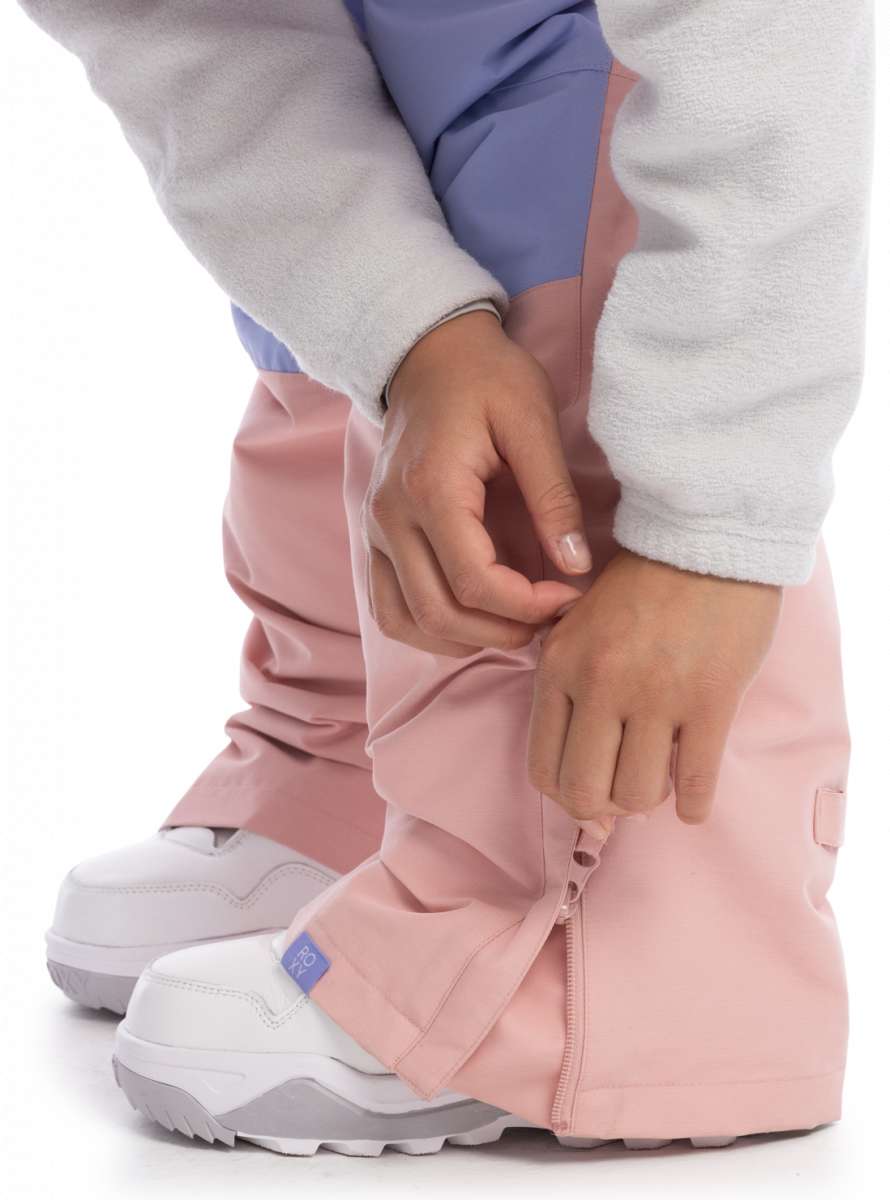 Roxy Women's Chloe Kim Bib Pant 2023 - A pair of pink snow pants with a blue stripe down the side, worn by a model in front view.