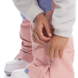 Roxy Women's Chloe Kim Bib Pant 2023 - A pair of pink snow pants with a blue stripe down the side, worn by a model in front view.