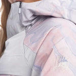 Roxy Women's Chloe Kim Overhead Jacket 2023 - A pastel pink jacket with a subtle marbled pattern and a white Nike swoosh logo on the left sleeve.