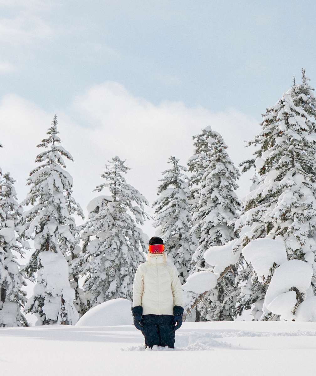 Roxy Women's Dusk Warmlink Insulated Jacket 2024 - A woman in a white jacket with black accents and a hood, standing on a snowy mountain slope.