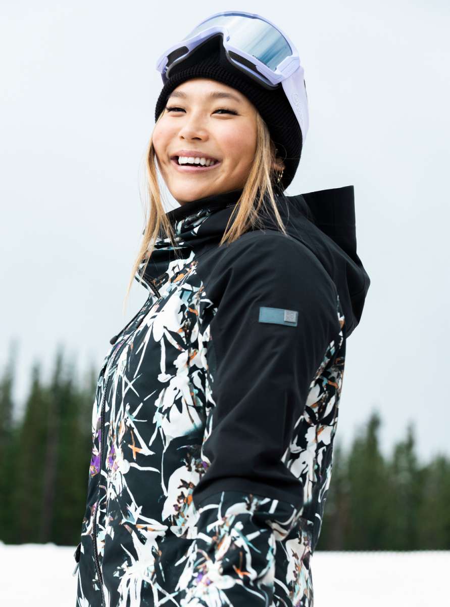 Roxy Women's Essence Gore-Tex Stretch Jacket 2022 - A black jacket with a white floral pattern and purple accents, worn by a model in front of a snowy background.