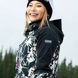 Roxy Women's Essence Gore-Tex Stretch Jacket 2022 - A black jacket with a white floral pattern and purple accents, worn by a model in front of a snowy background.