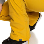 Roxy Women's Rising High Pant 2023 - A pair of yellow snow pants with a zippered pocket on the side and a small black tag near the hem.