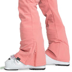 Roxy Women's Rising High Pant 2024 - A pair of pink snow pants with a zippered pocket on the side and a black tag near the bottom hem.