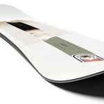 Salomon Women's Bliss Snowboard 2024 - A white snowboard with a black stripe and a woman riding it in the background.