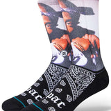 Stance Makaveli Crew Sock 2023 - A pair of crew socks feature a large image of Tupac Shakur's face on the top portion, with his hand raised to his chin and wearing a black bandana wrapped around his head.