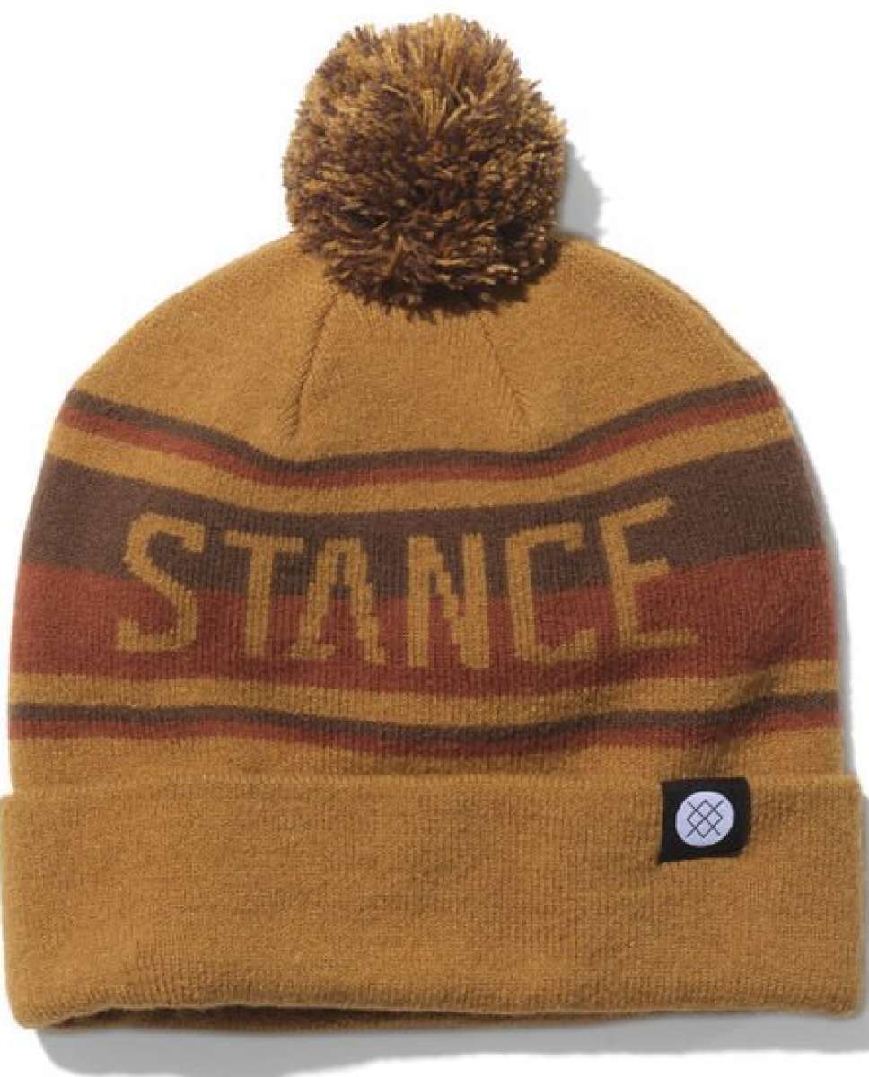 Stance OG Pom Beanie 2023 - A tan beanie with a brown pom-pom on top and a repeating pattern of red, yellow, and gray stripes around it.