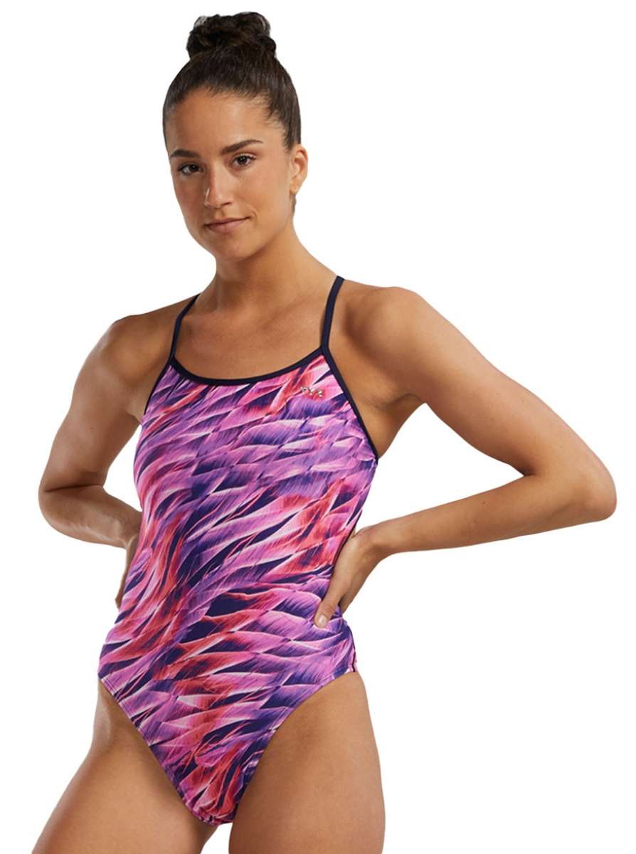 TYR Women's Trinifyfit Falcon Swimsuit - A pink, purple, and white swimsuit with a geometric pattern on a woman standing in front of a plain background.