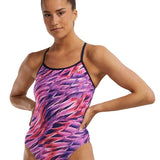 TYR Women's Trinifyfit Falcon Swimsuit - A pink, purple, and white swimsuit with a geometric pattern on a woman standing in front of a plain background.