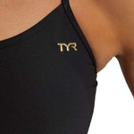 TYR Women's Trinityfit Torch Swimsuit - A black swimsuit with a gold logo on the upper left side of the chest area.