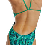 TYR Women's Crystalized Cutout Swimsuit - A woman in a green swimsuit with cutouts on the sides, posing from behind and slightly to her right.