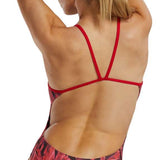 TYR Women's Crystalized Cutout Swimsuit - A red swimsuit with a geometric pattern of darker red and black triangles, worn by a woman from behind, facing left.