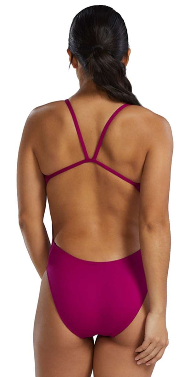 TYR Women's Solid Cutoutfit Swimsuit - A woman with long dark hair in a low ponytail, wearing a magenta swimsuit with thin straps and cutouts on the sides.