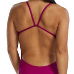 TYR Women's Solid Cutoutfit Swimsuit - A woman with long dark hair in a low ponytail, wearing a magenta swimsuit with thin straps and cutouts on the sides.