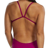 TYR Women's Solid Cutoutfit Swimsuit - A woman with long dark hair in a low ponytail, wearing a magenta swimsuit with thin straps and cutouts on the sides.