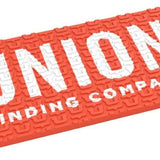 Union Surf Stomp Pad - A coral-colored pad with a textured surface, featuring a repeating pattern of stylized "U" shapes and the word "UNION" in white letters at the top.
