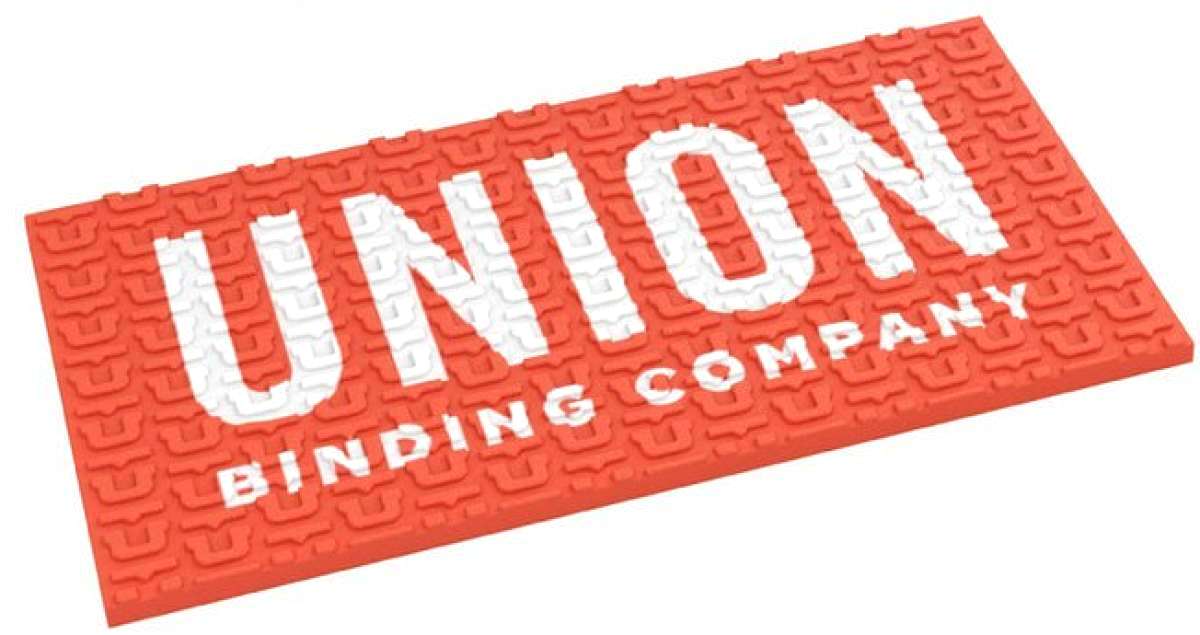 Union Surf Stomp Pad - A coral-colored pad with a textured surface, featuring a repeating pattern of stylized "U" shapes and the word "UNION" in white letters at the top.