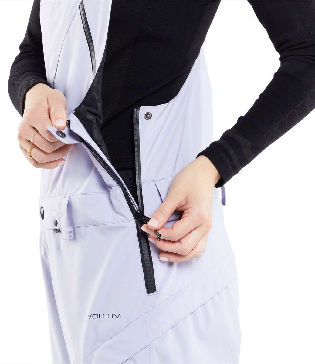 Volcom Women's Elm Stretch GORE-TEX Bib Pant - A pair of white snow pants with a black zipper and snap buttons, featuring a diagonal pattern on the side pocket.