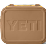 Yeti Hopper Flip 12 Personal Cooler - A tan cooler with a black zipper and handle on top, featuring an embossed "YETI" logo in the center of the lid.
