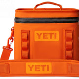 Yeti Hopper Flip 8 Personal Cooler - A small, portable cooler with a handle and wheels for easy transport. It has an orange color and is made of durable material. The brand logo "YETI" is prominently displayed on the front.